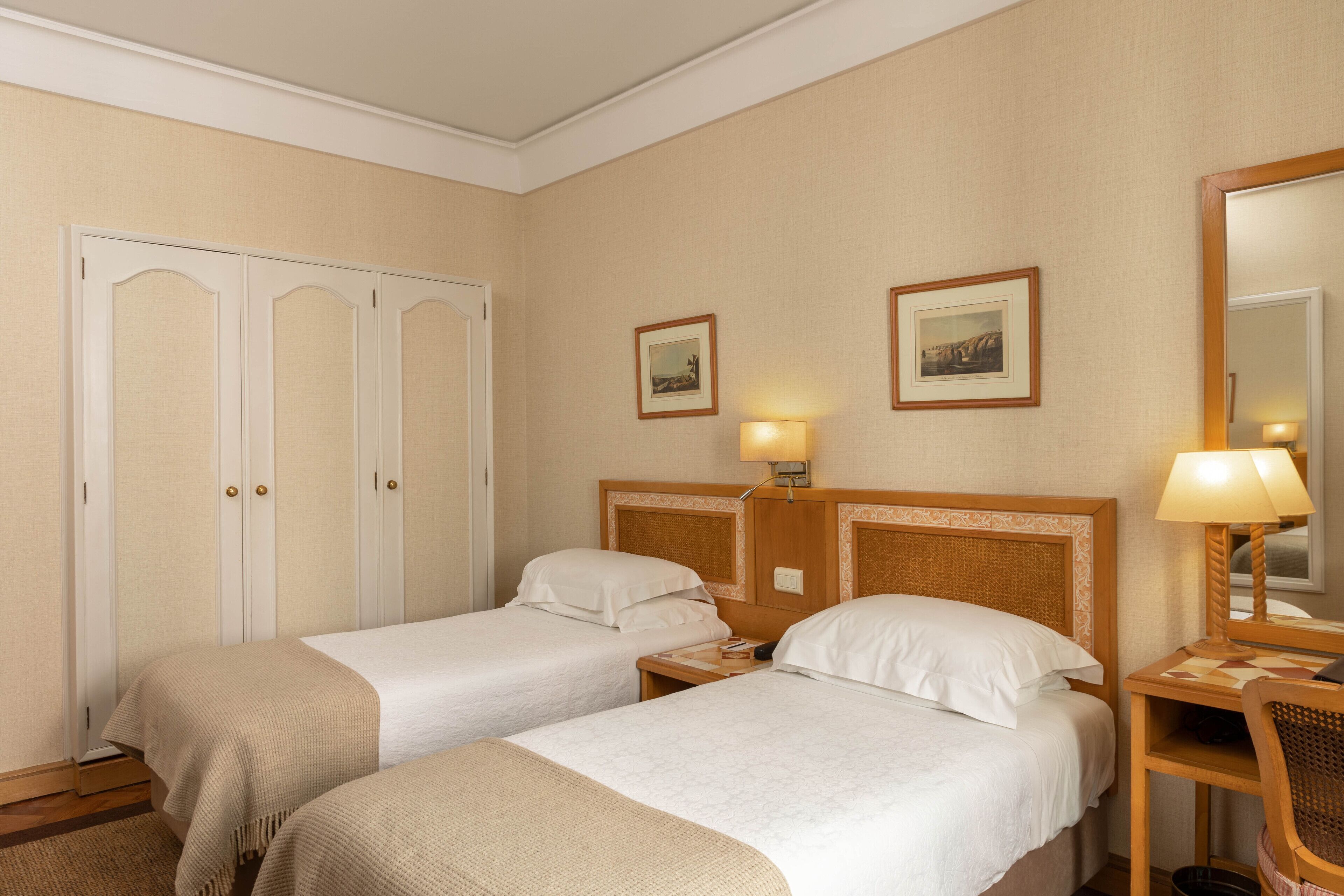 Une chambre d’hôtel avec deux lits simples, une armoire, une table de chevet avec une lampe et un miroir.