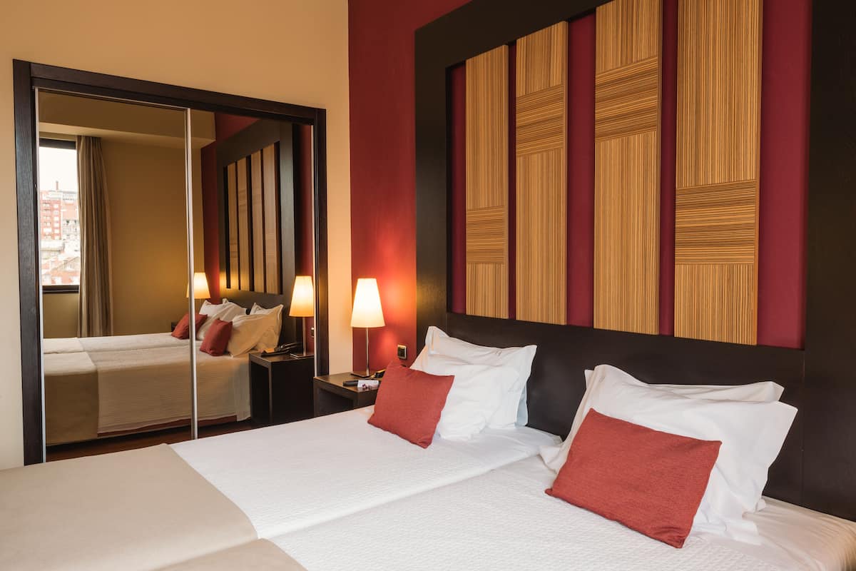 A hotel room with a large bed, a nightstand with a lamp, a mirror, and a wall with a geometric pattern.