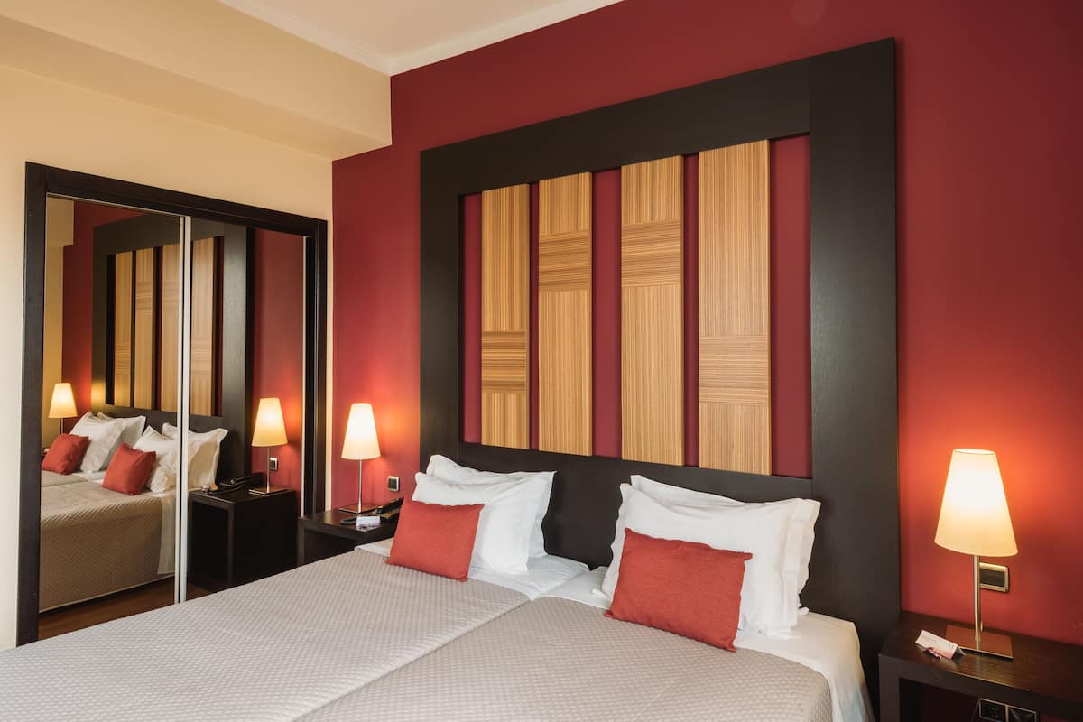 A hotel room with a large bed, two bedside tables with lamps, a mirror, and a red accent wall.