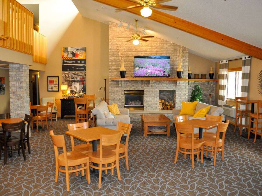 A spacious living area with a fireplace, a television mounted on a brick wall, and multiple seating arrangements including a sofa and dining tables.