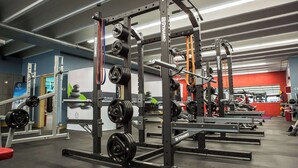 Un gimnasio con equipo de levantamiento de pesas, bancos y una pared roja al fondo.