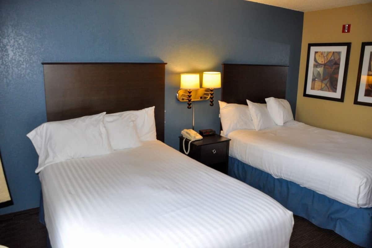 A hotel room with two beds, a nightstand with a phone, and wall-mounted lamps.