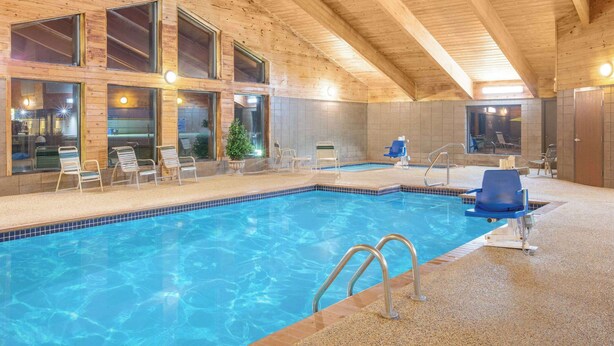 Una piscina interior con agua azul cristalina, vigas de madera en el techo y amplias ventanas.