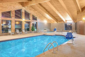 Una piscina interior con agua azul cristalina, vigas de madera en el techo y amplias ventanas.