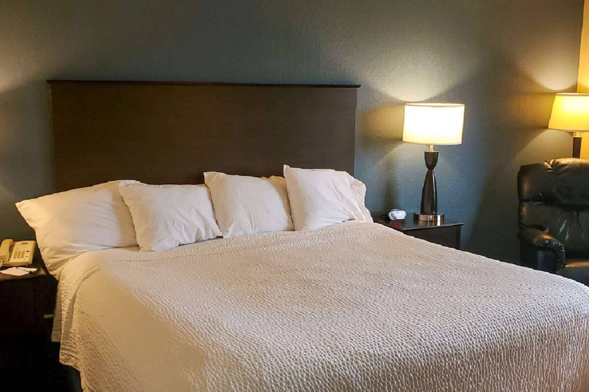 A hotel room with a large bed, a nightstand with a lamp, and a leather chair.