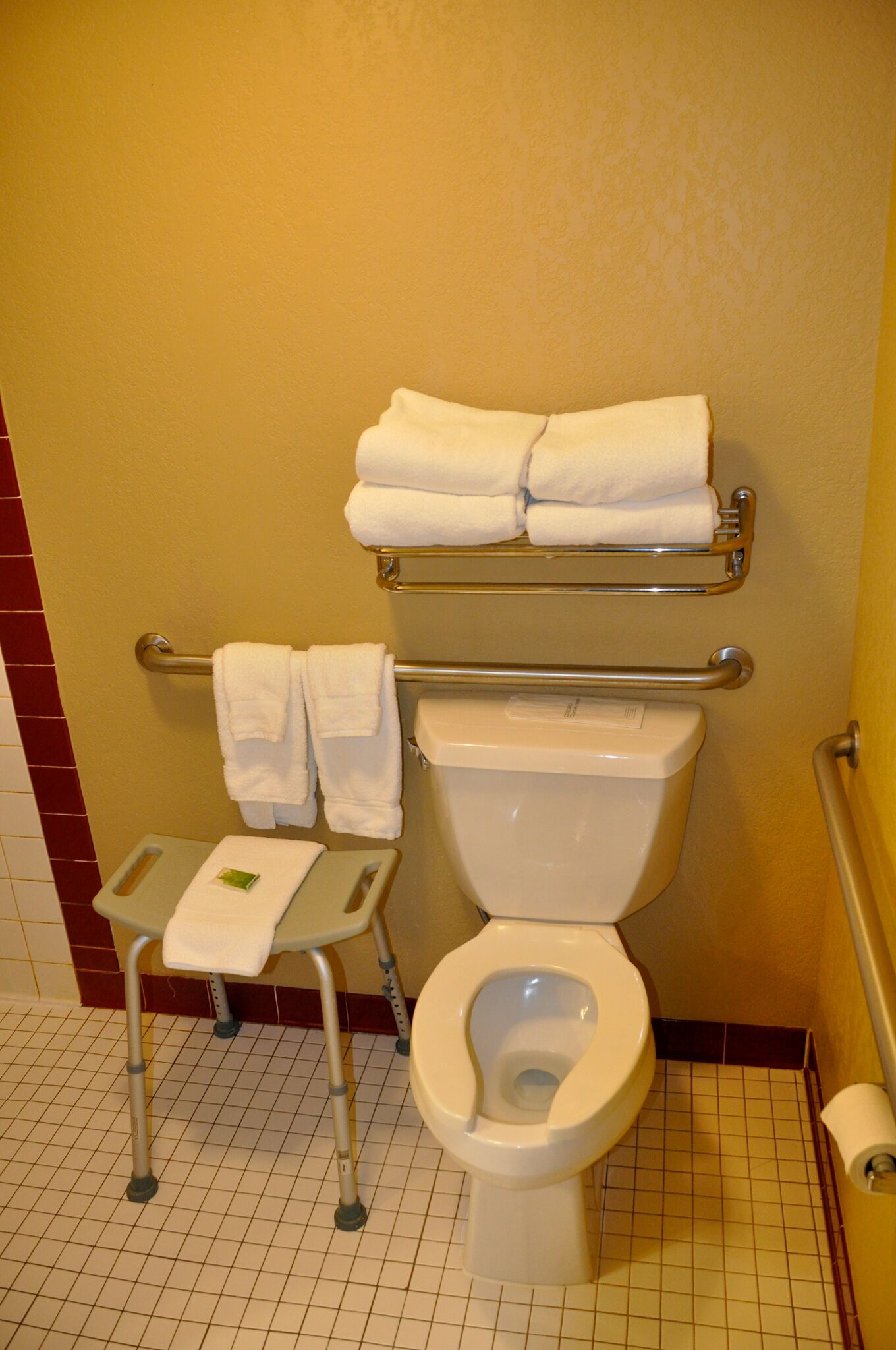 A bathroom with a toilet, a handrail, and a small chair with a towel.