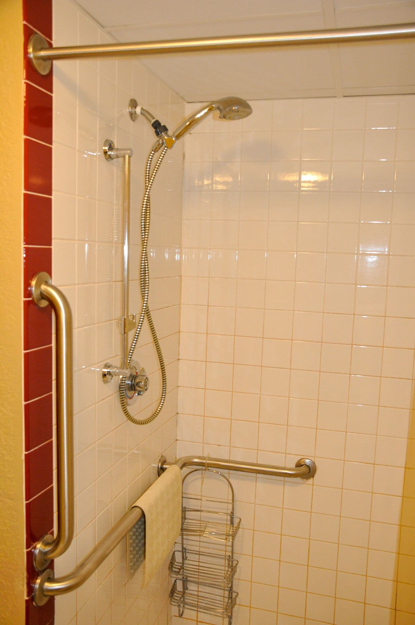 Uma área de chuveiro com barra de apoio, chuveiro manual e porta-toalhas.