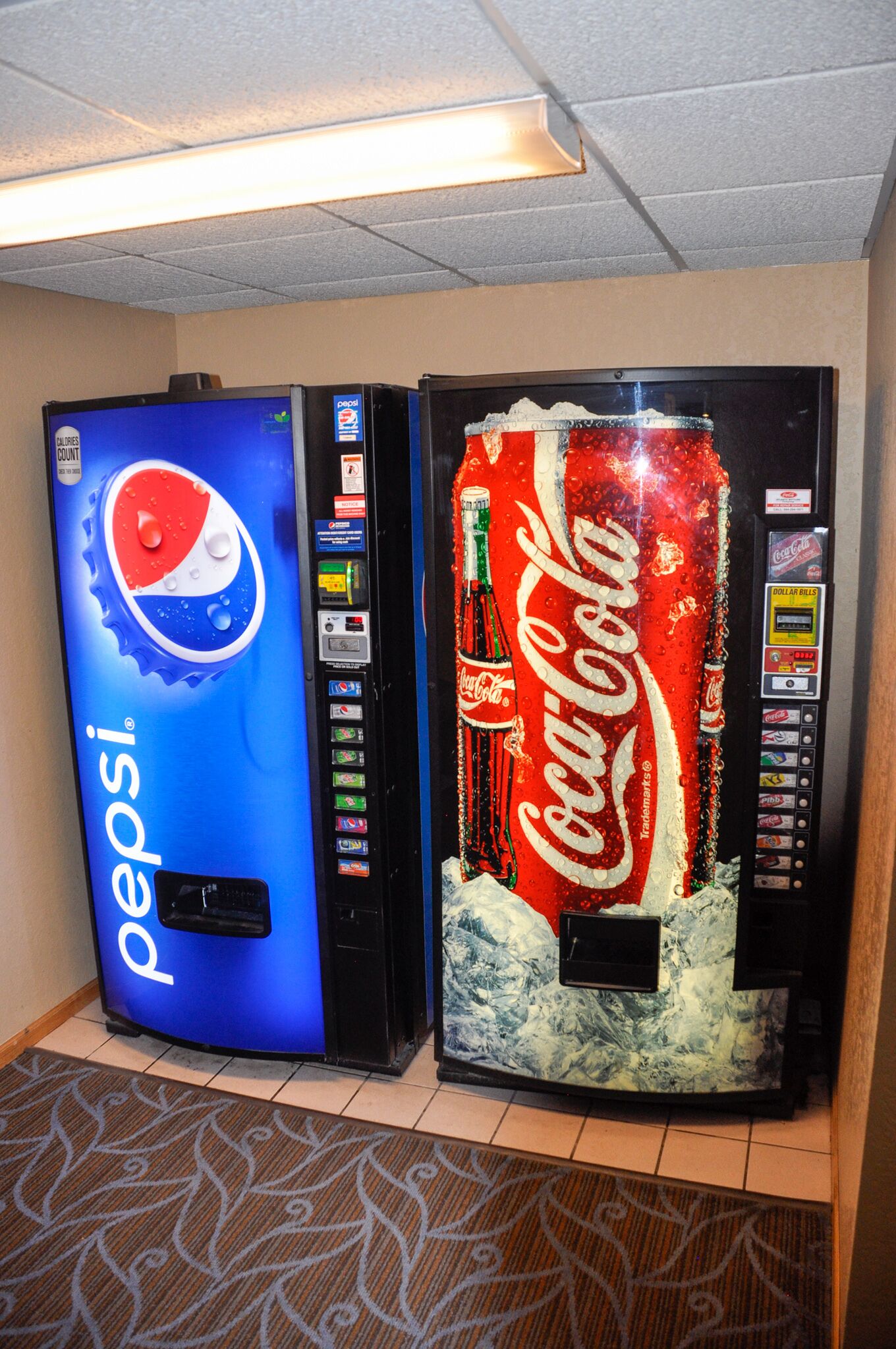 Dues màquines expenedores, una de Pepsi i una de Coca-Cola, en una habitació amb un paviment decorat.