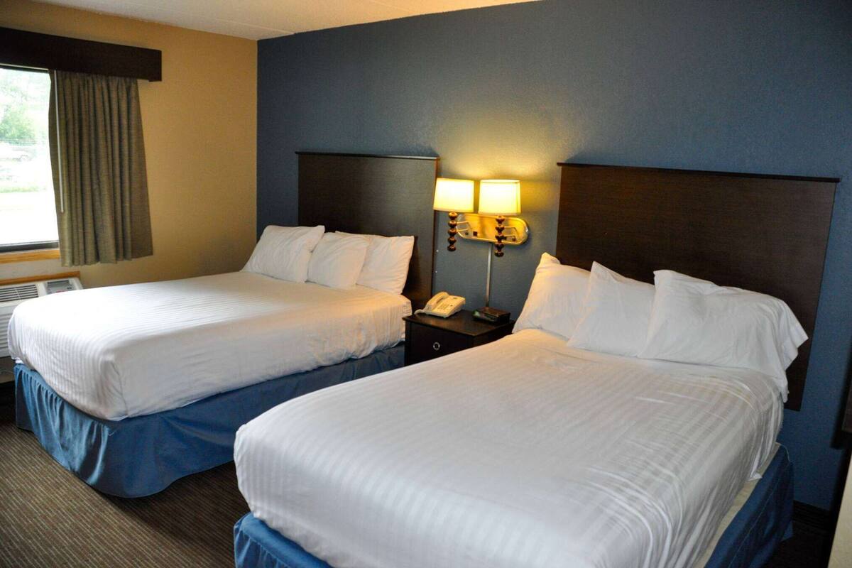 A hotel room with two beds, a nightstand with a lamp, and a window with curtains.