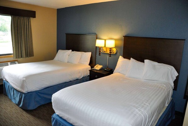 Una habitación de hotel con dos camas, una mesita de noche con lámpara y una ventana con cortinas.