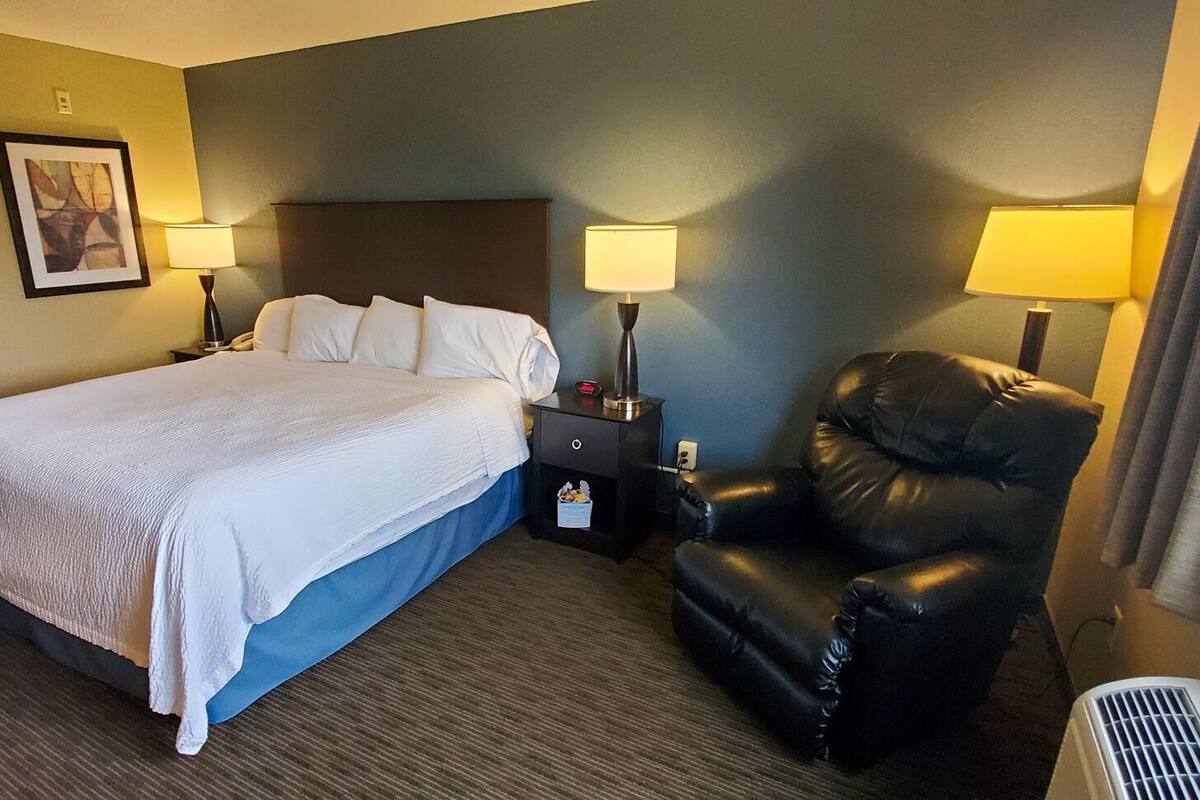 A hotel room with a bed, two bedside lamps, a chair, and two framed pictures on the wall.