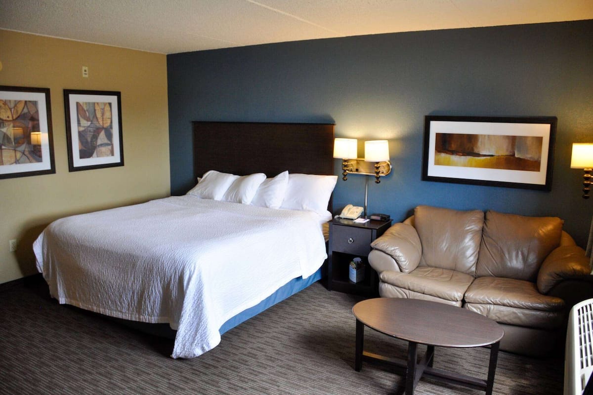 A hotel room with a large bed, a leather sofa, a small table, and two wall-mounted lamps.