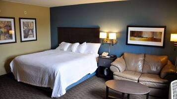 A hotel room with a large bed, a leather sofa, a small table, and two wall-mounted lamps.