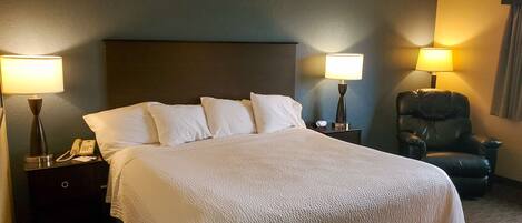 A hotel room with a bed, two bedside lamps, a telephone, a chair, and a nightstand.