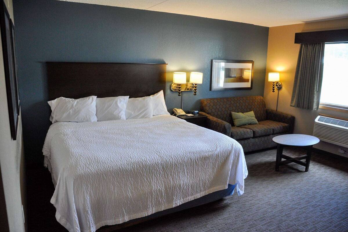A hotel room with a large bed, a sofa, a small table, and two wall-mounted lamps.