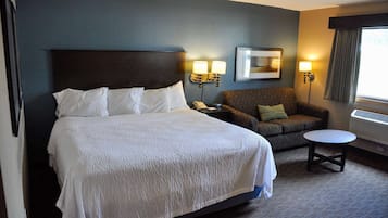 A hotel room with a large bed, a sofa, a small table, and two wall-mounted lamps.