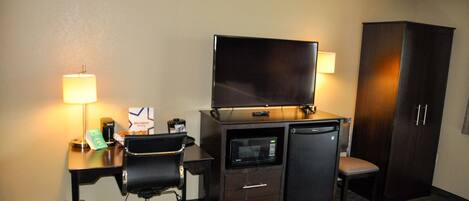 A hotel room with a desk, chair, television, microwave, and a wardrobe.
