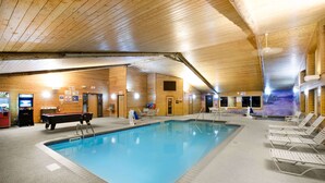 An indoor swimming pool with a wooden ceiling and walls, poolside lounge chairs, and a pool table.