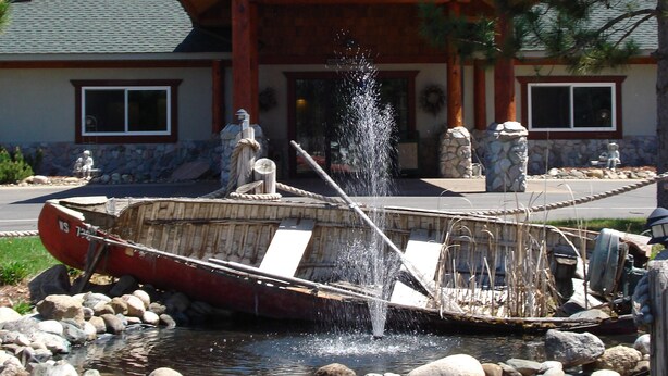 A rustic lodge with a stone facade, a wooden porch, and a small boat in the foreground.