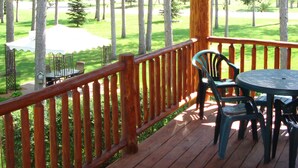 A wooden deck with a table and chairs, overlooking a grassy area with trees.