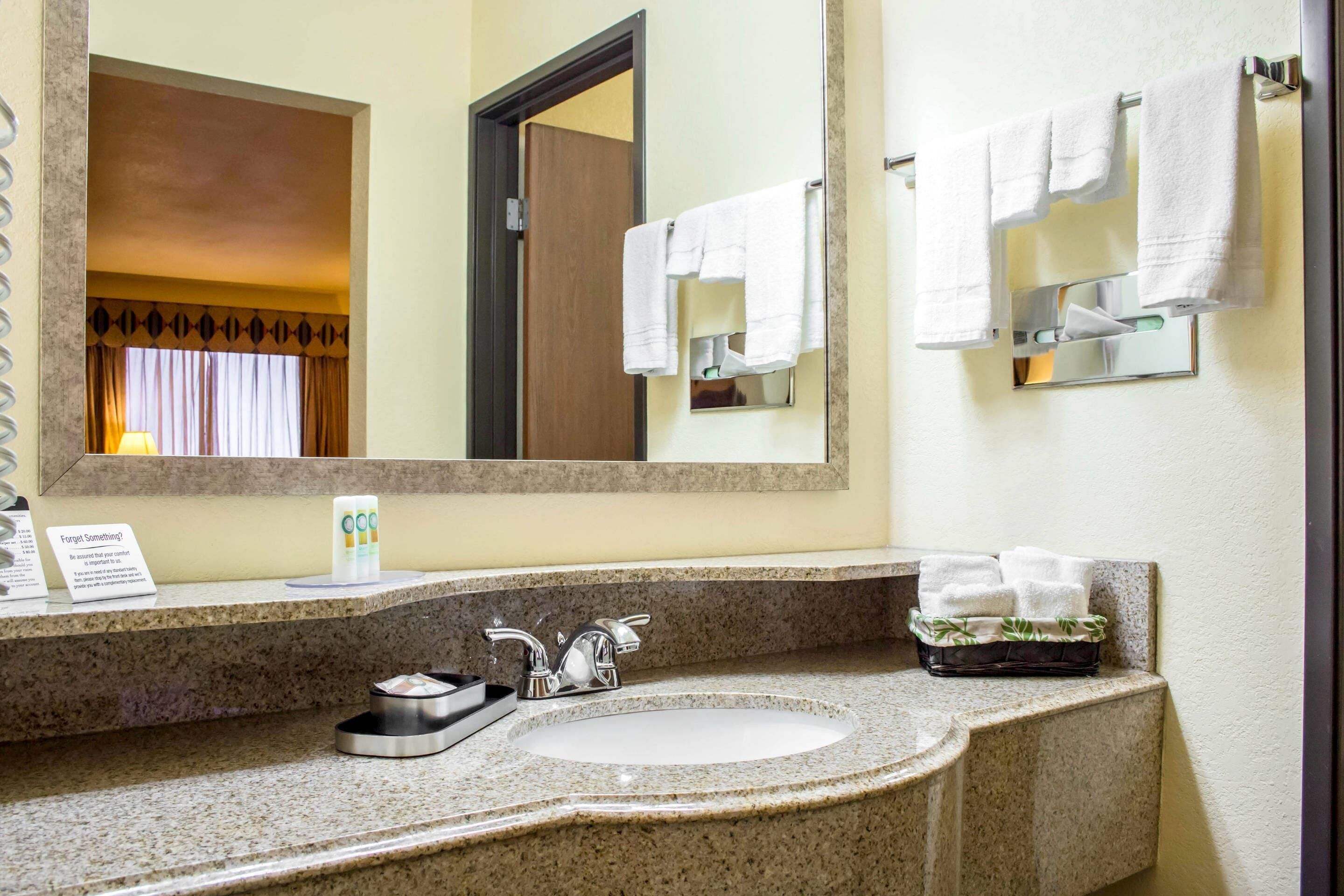 A hotel bathroom with a granite countertop, a sink, a mirror, and a towel rack.