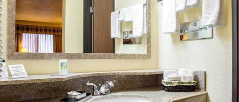 A hotel bathroom with a granite countertop, a sink, a mirror, and a towel rack.