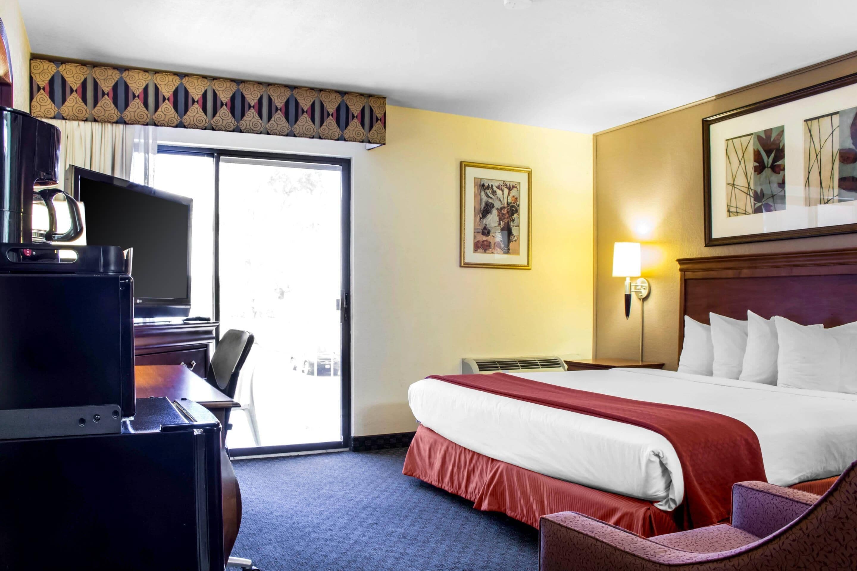 A hotel room with a bed, desk, chair, and a television.