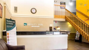 Un comptoir d’accueil avec une horloge, une enseigne indiquant « Quality Inn », et un escalier.