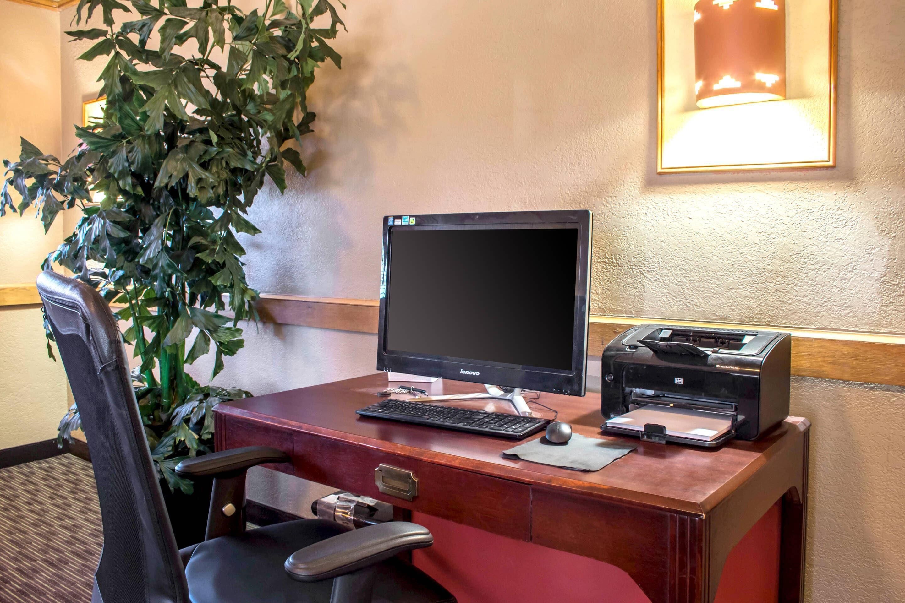A hotel desk with a computer, printer, and chair.