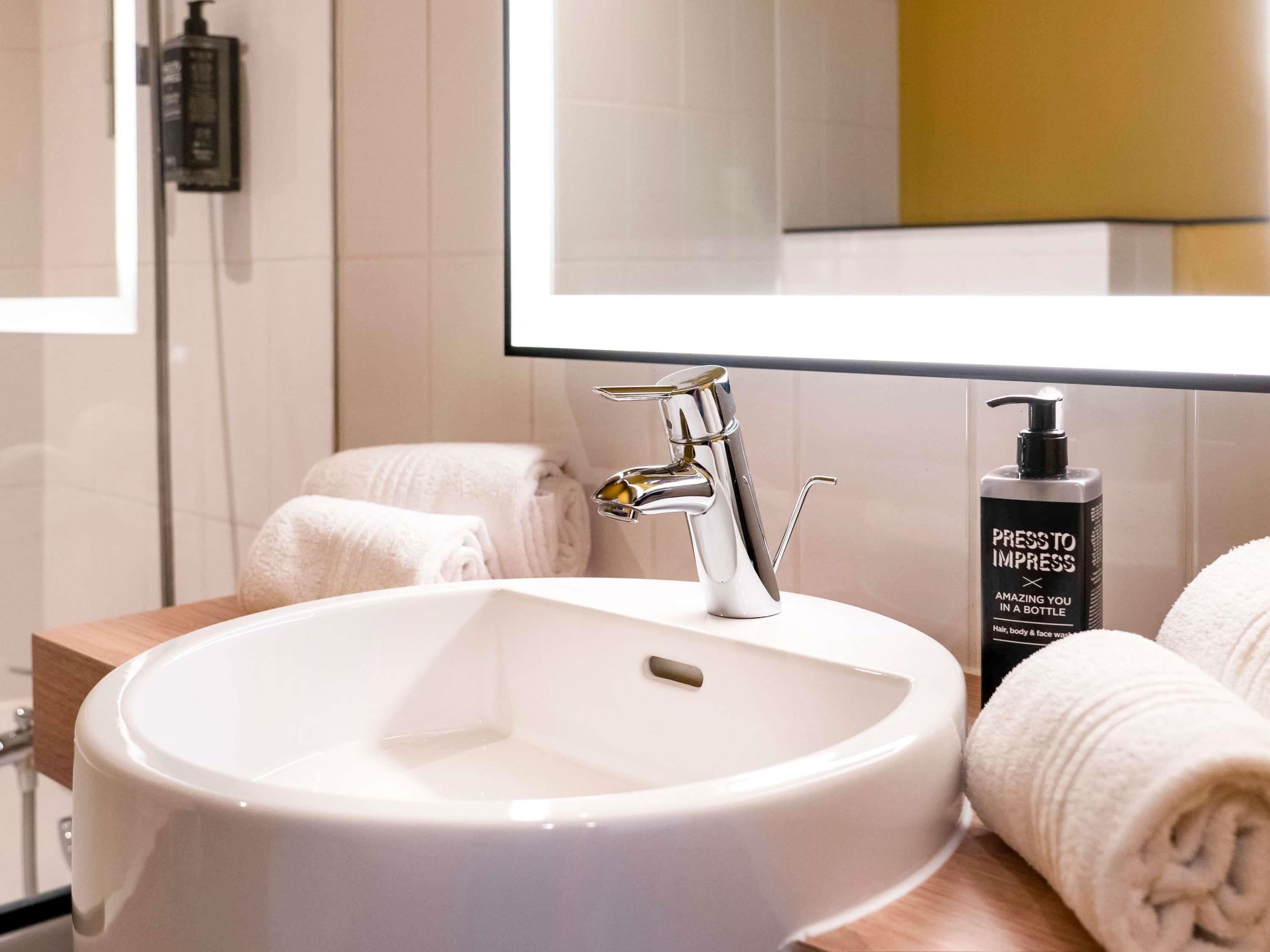 Une salle de bain avec un lavabo blanc, un miroir et une bouteille de shampoing.