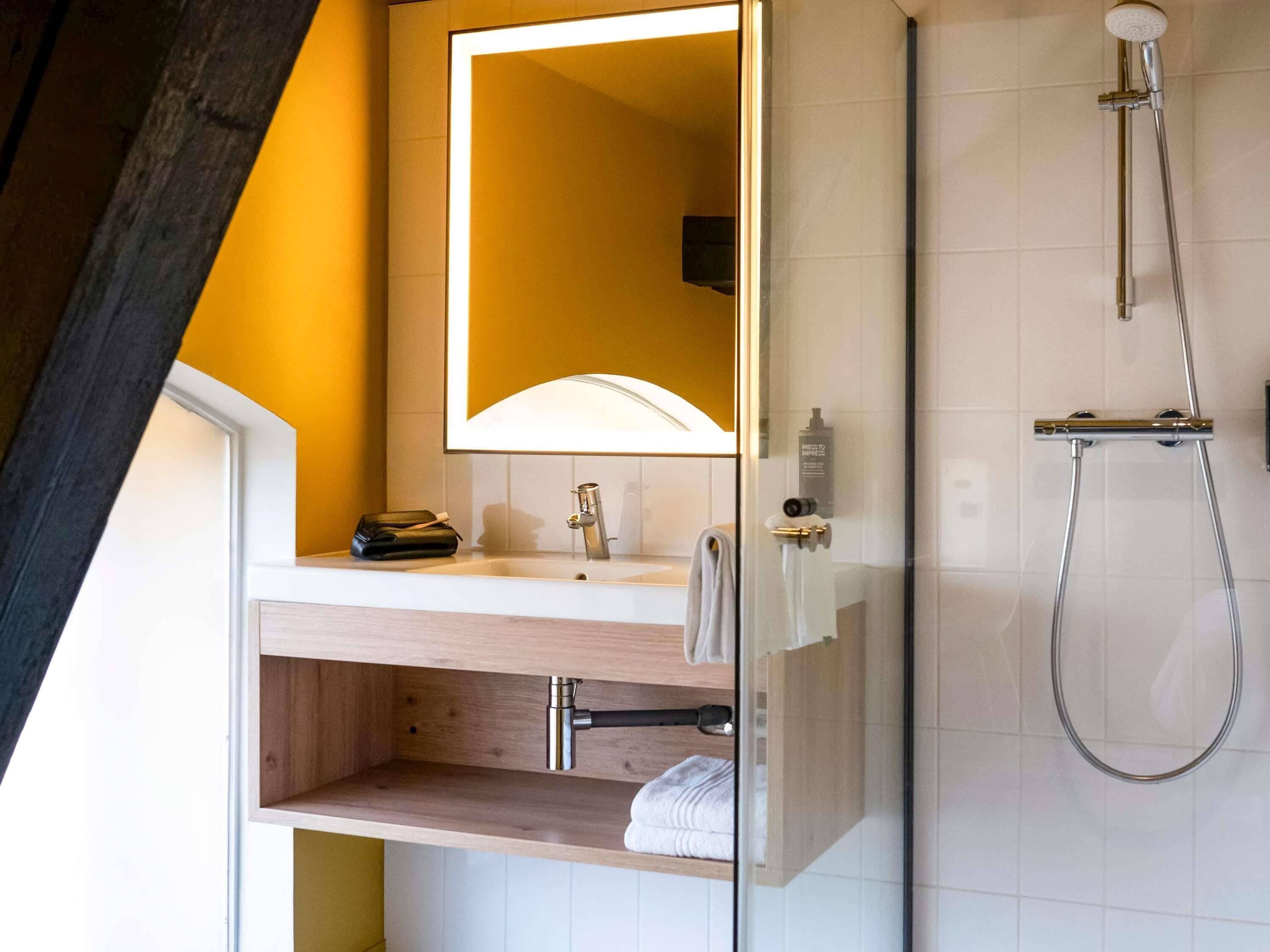 A modern bathroom with a wooden vanity, a mirror, a shower, and a towel rack.