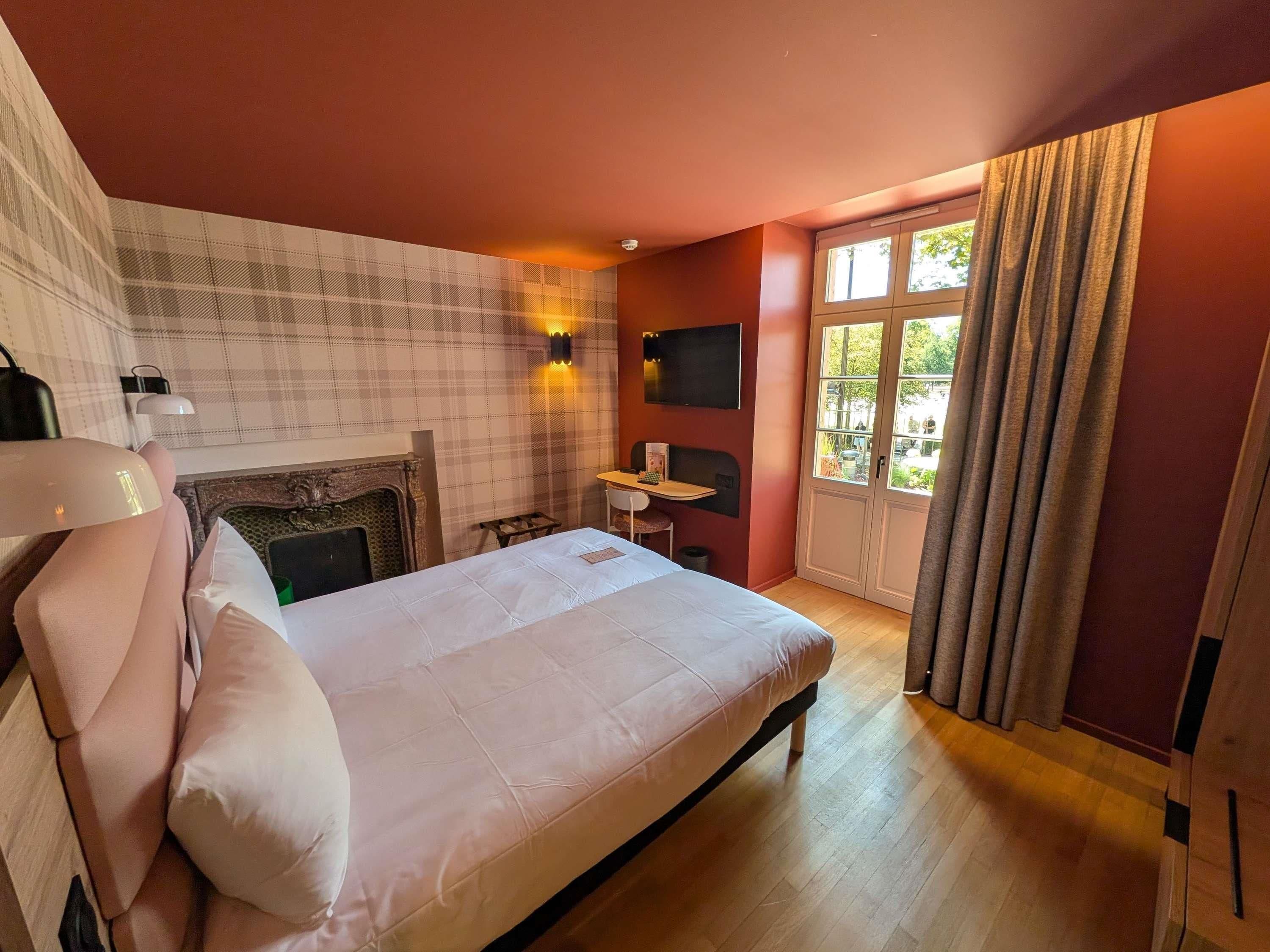 Ein Hotelzimmer mit einem Bett, einem Schreibtisch, einem Kamin, einem Fernseher und einem Fenster mit Vorhängen.
