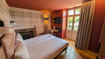 Ein Hotelzimmer mit einem Bett, einem Schreibtisch, einem Kamin, einem Fernseher und einem Fenster mit Vorhängen.