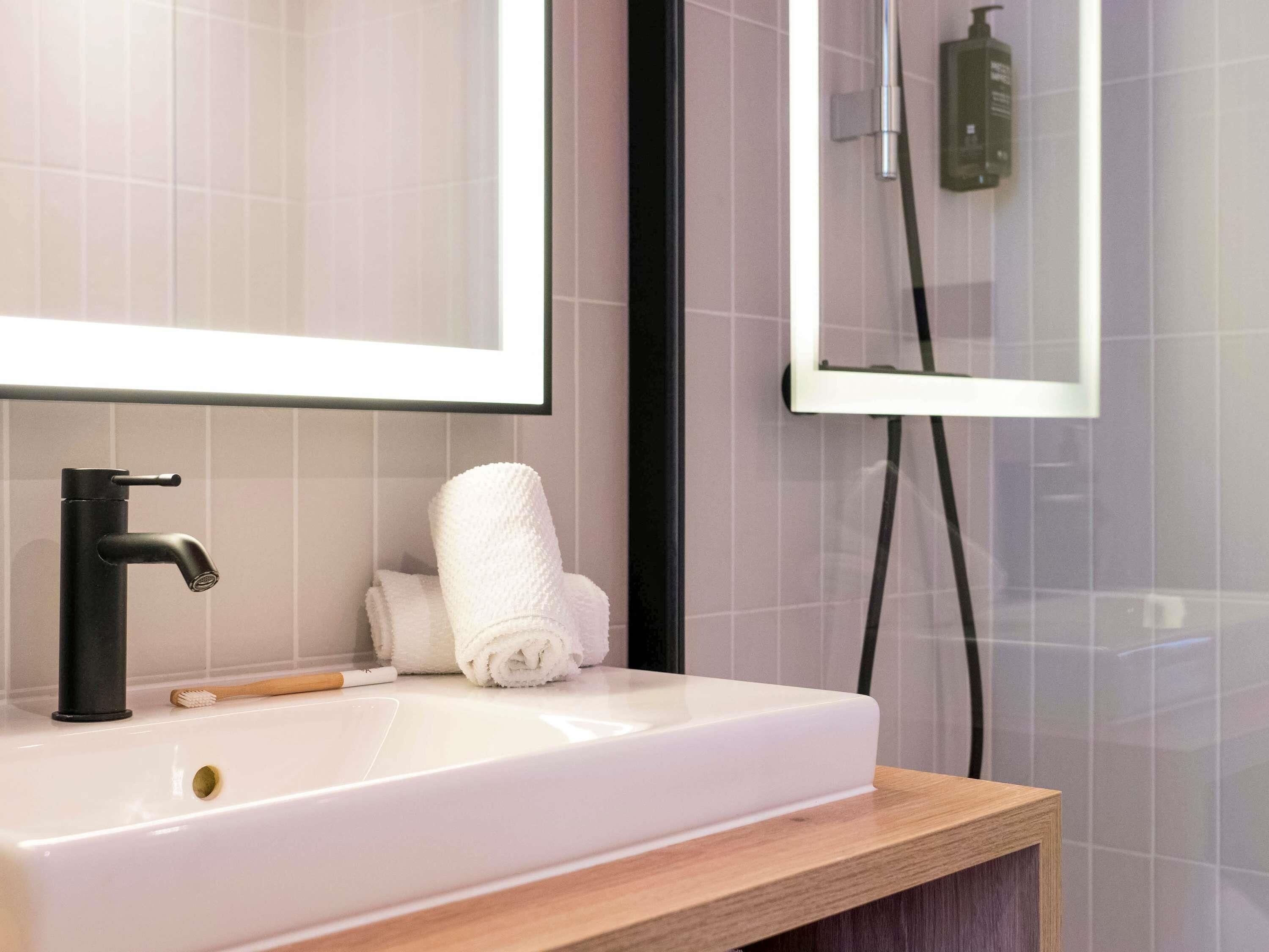 Een badkamer met een witte wasbak, een zwarte kraan, een houten wastafelmeubel en een handdoek.