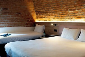 Una habitación de hotel con dos camas, una pared de ladrillo y un cabecero de madera.