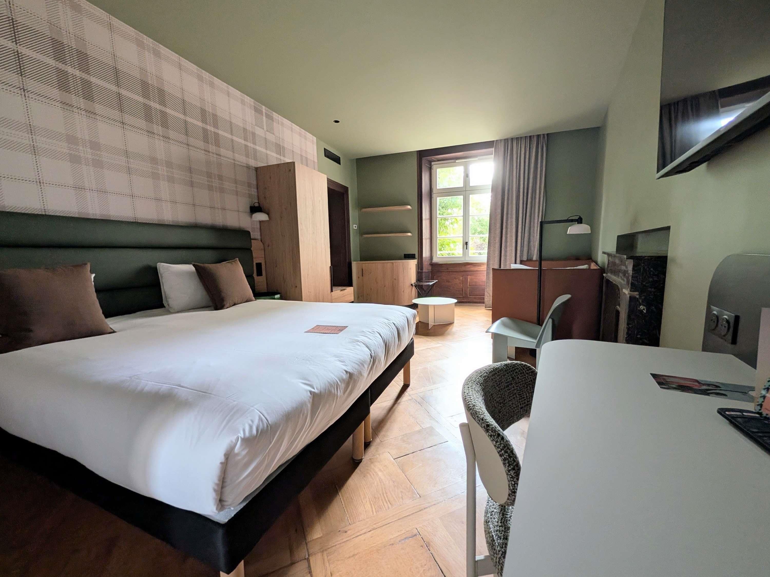 Une chambre d’hôtel avec un grand lit, un bureau, une chaise, une télévision et une fenêtre avec des rideaux.