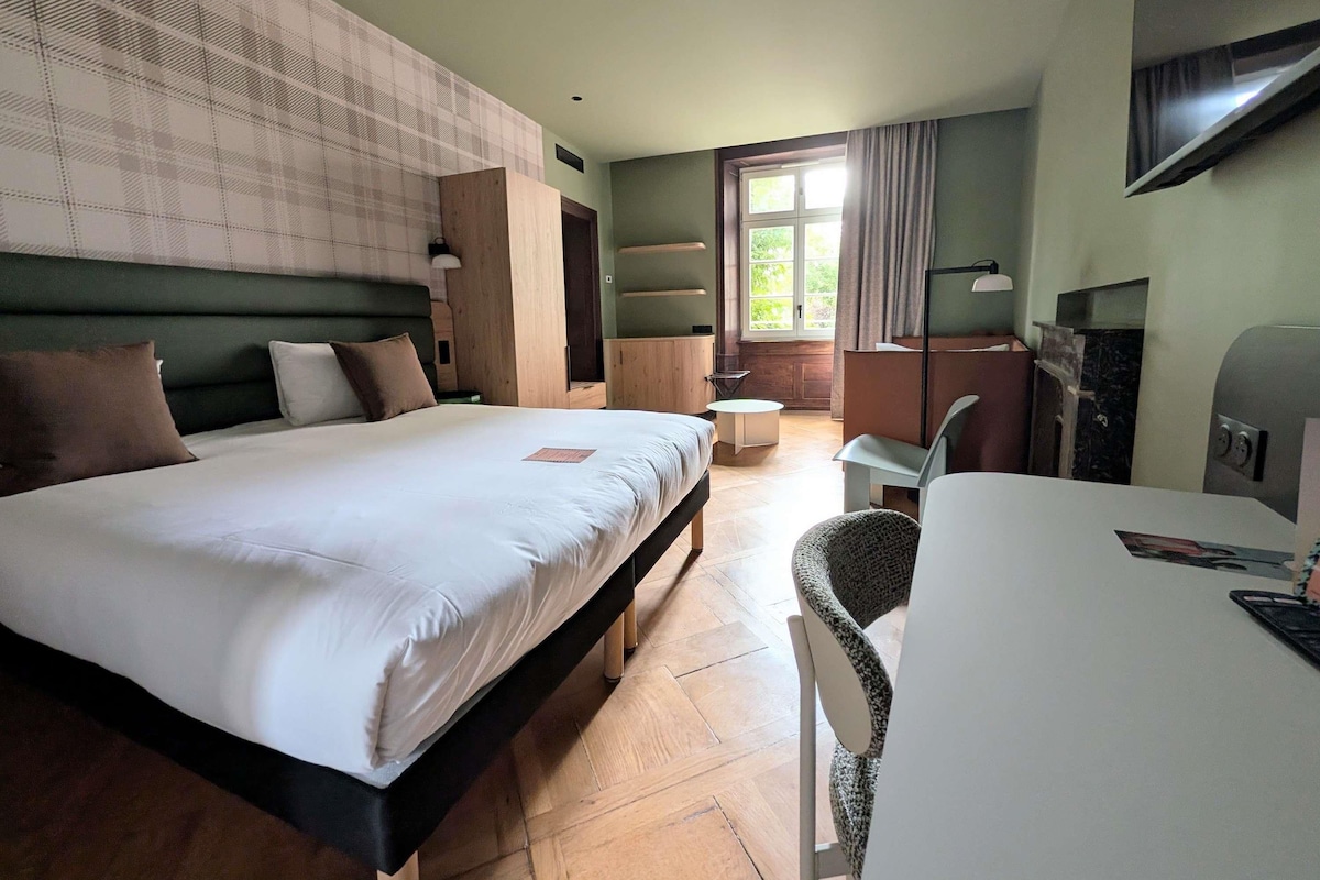 A hotel room with a large bed, a desk, a chair, a television, and a window with curtains.