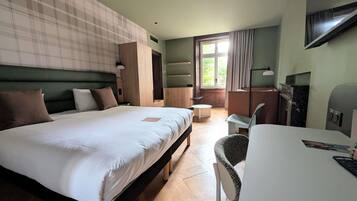 Une chambre d’hôtel avec un grand lit, un bureau, une chaise, une télévision et une fenêtre avec des rideaux.