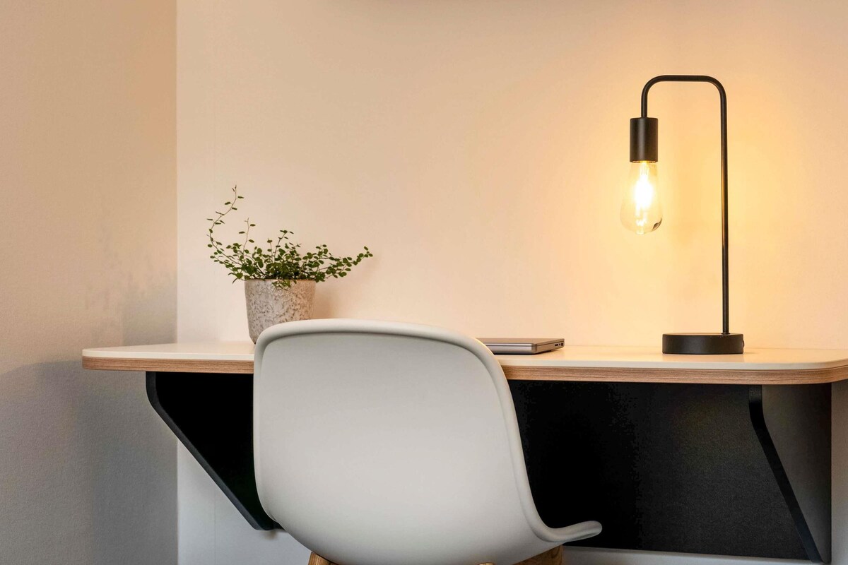 A modern desk with a laptop, a potted plant, and a desk lamp.