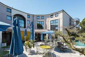 A modern outdoor patio area with tables and chairs, umbrellas, and a pool. - Radisson Hotel Aix en Provence (Aix-en-Provence)