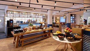 A modern cafe with a wooden table set for breakfast, a bar area with various beverages, and a seating area with a view. - Radisson Hotel Aix en Provence (Aix-en-Provence)