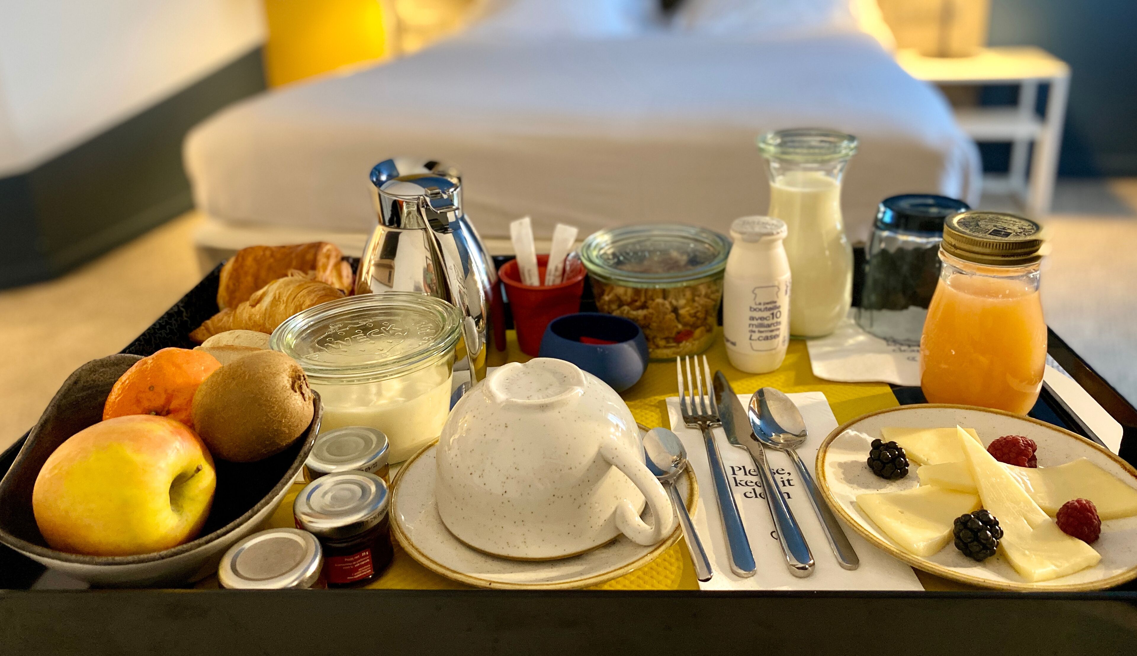 A breakfast tray with croissants, fruits, cheese, and beverages.