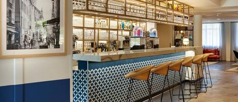 A bar area with a patterned backsplash, shelves with bottles, glasses, and a coffee machine.