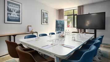 Een vergaderruimte met een grote tafel, blauwe stoelen, een projectiescherm en foto's in lijsten aan de muur.