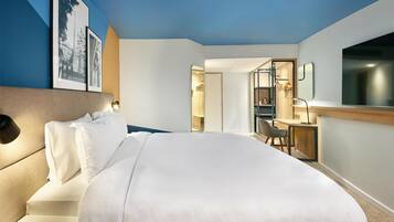 Habitación de hotel con una cama grande, un escritorio y una silla. Hay un cuadro enmarcado en la pared y un espejo en la pared opuesta.