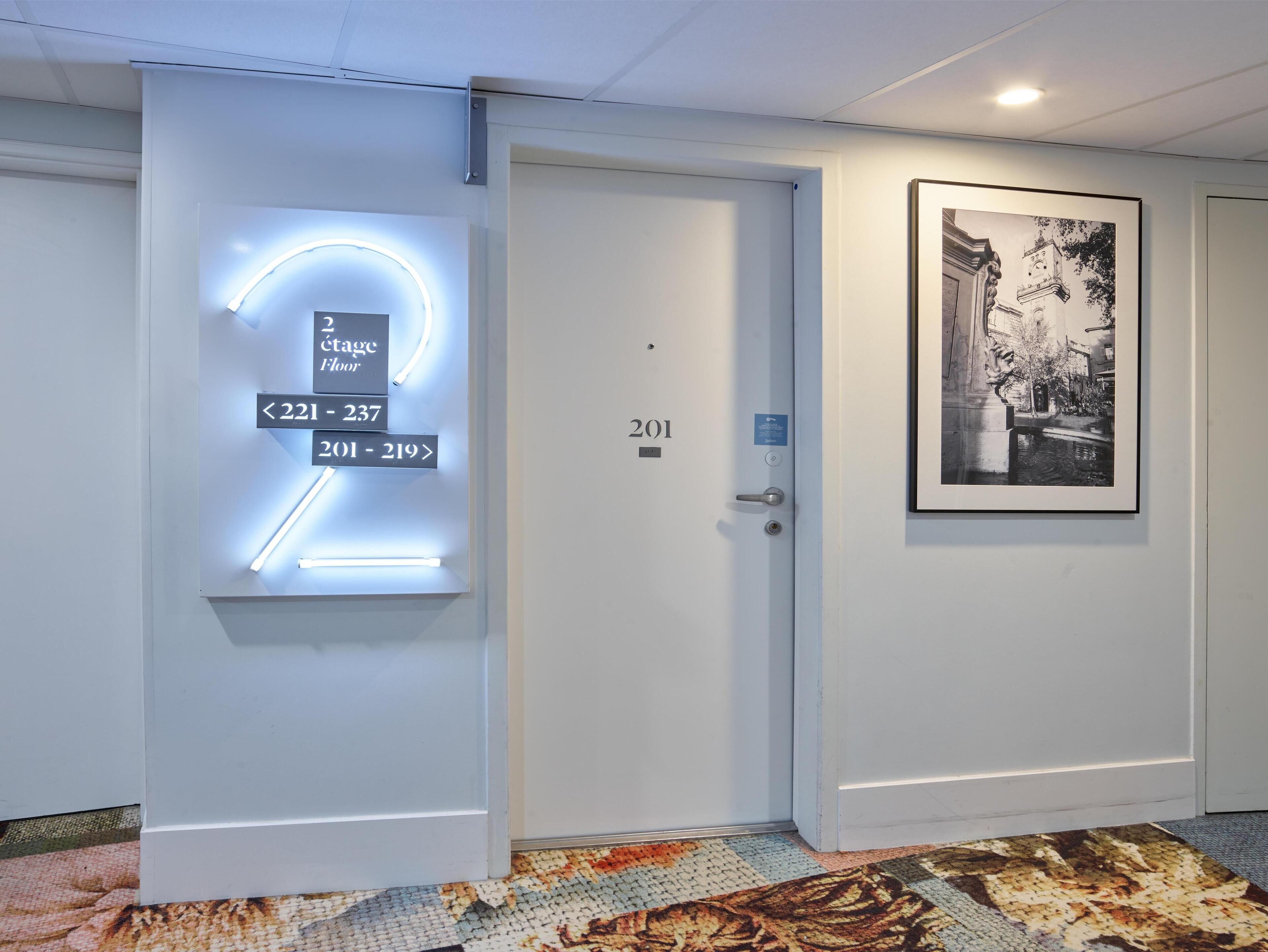 A hotel entrance with a modern illuminated sign indicating room numbers 201-219 and 2nd floor.