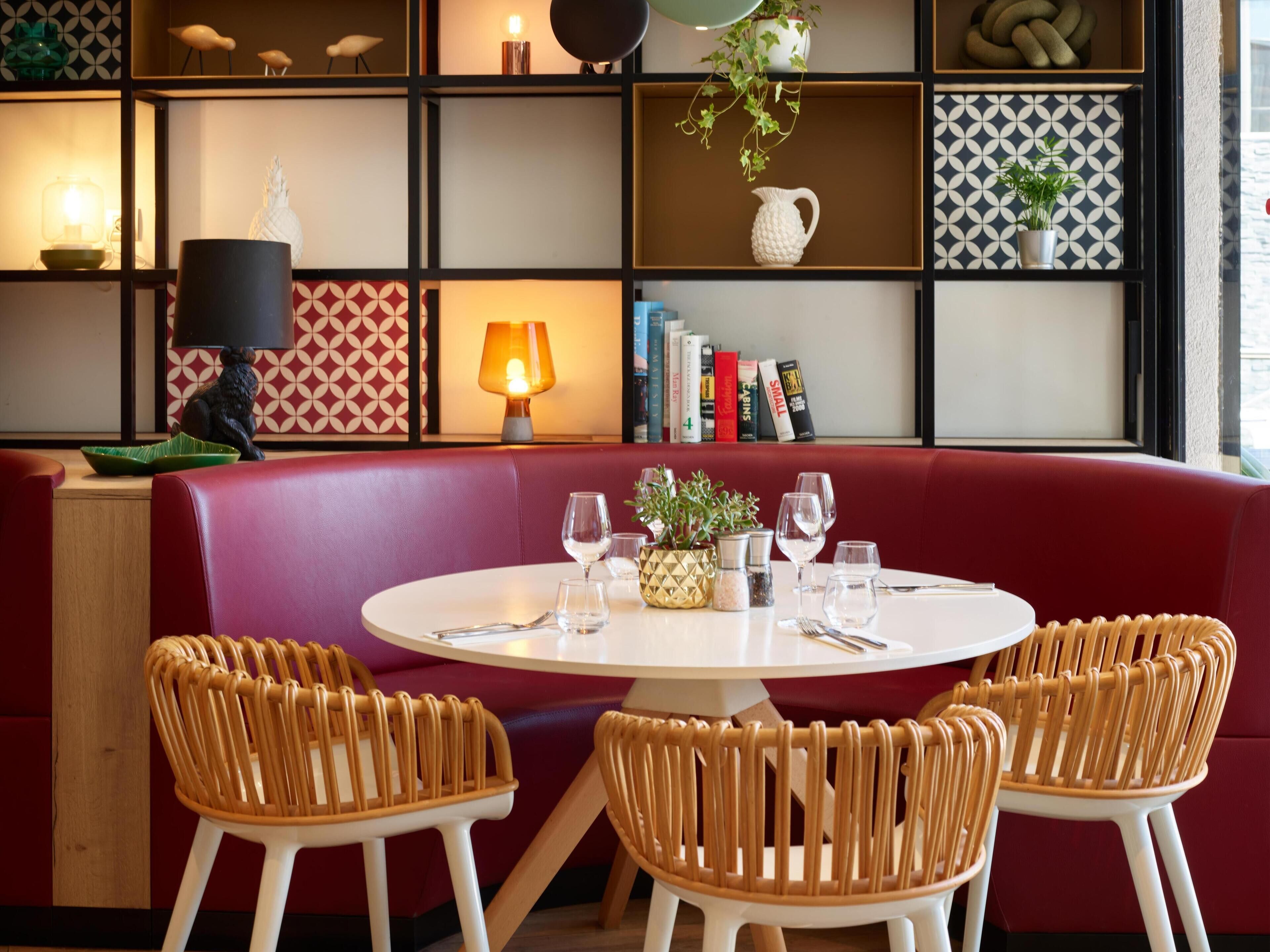 A dining area with a round table, wicker chairs, and a red cushioned bench.