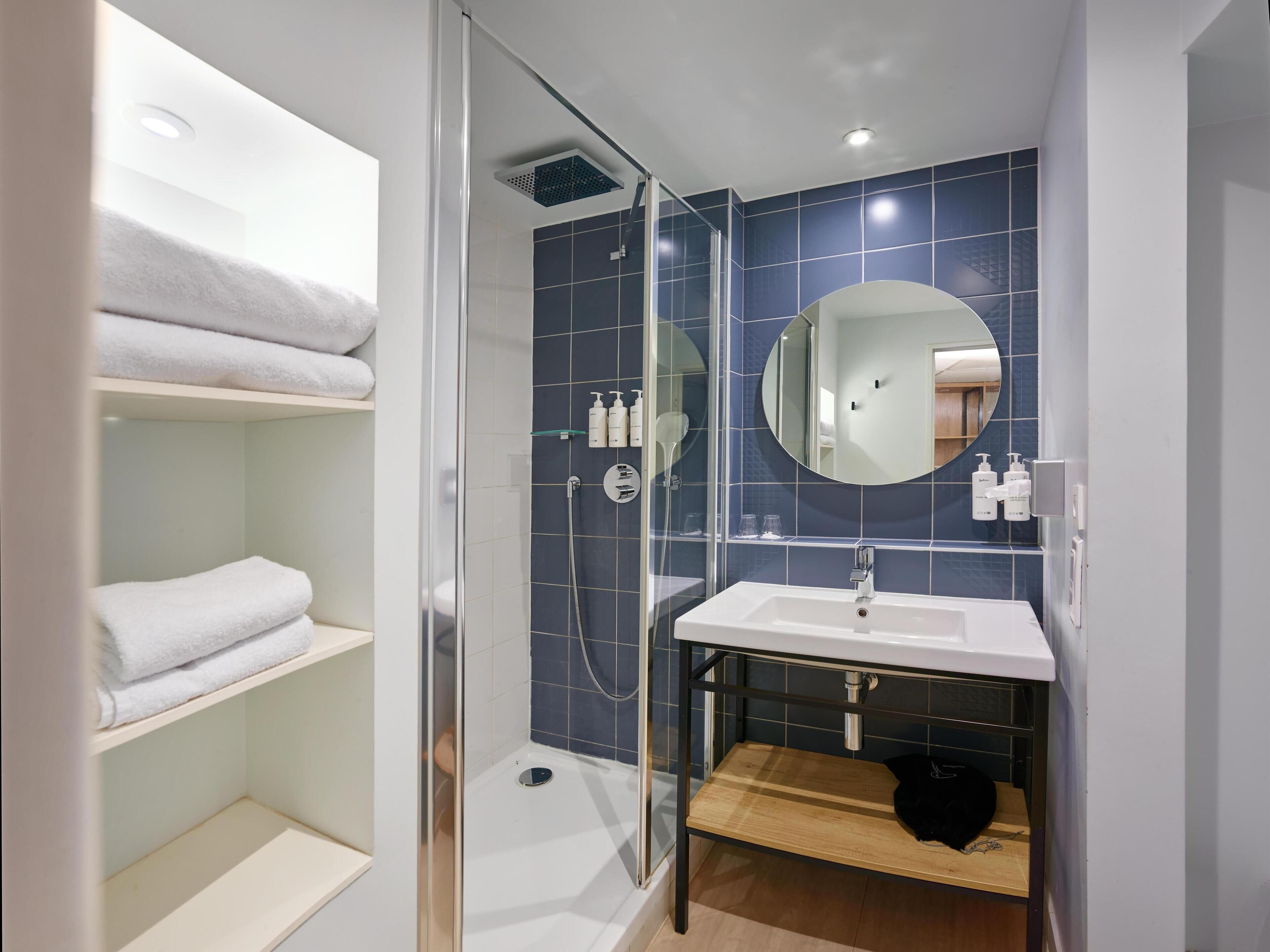 A modern bathroom with a glass-enclosed shower, a white sink, and a mirror.