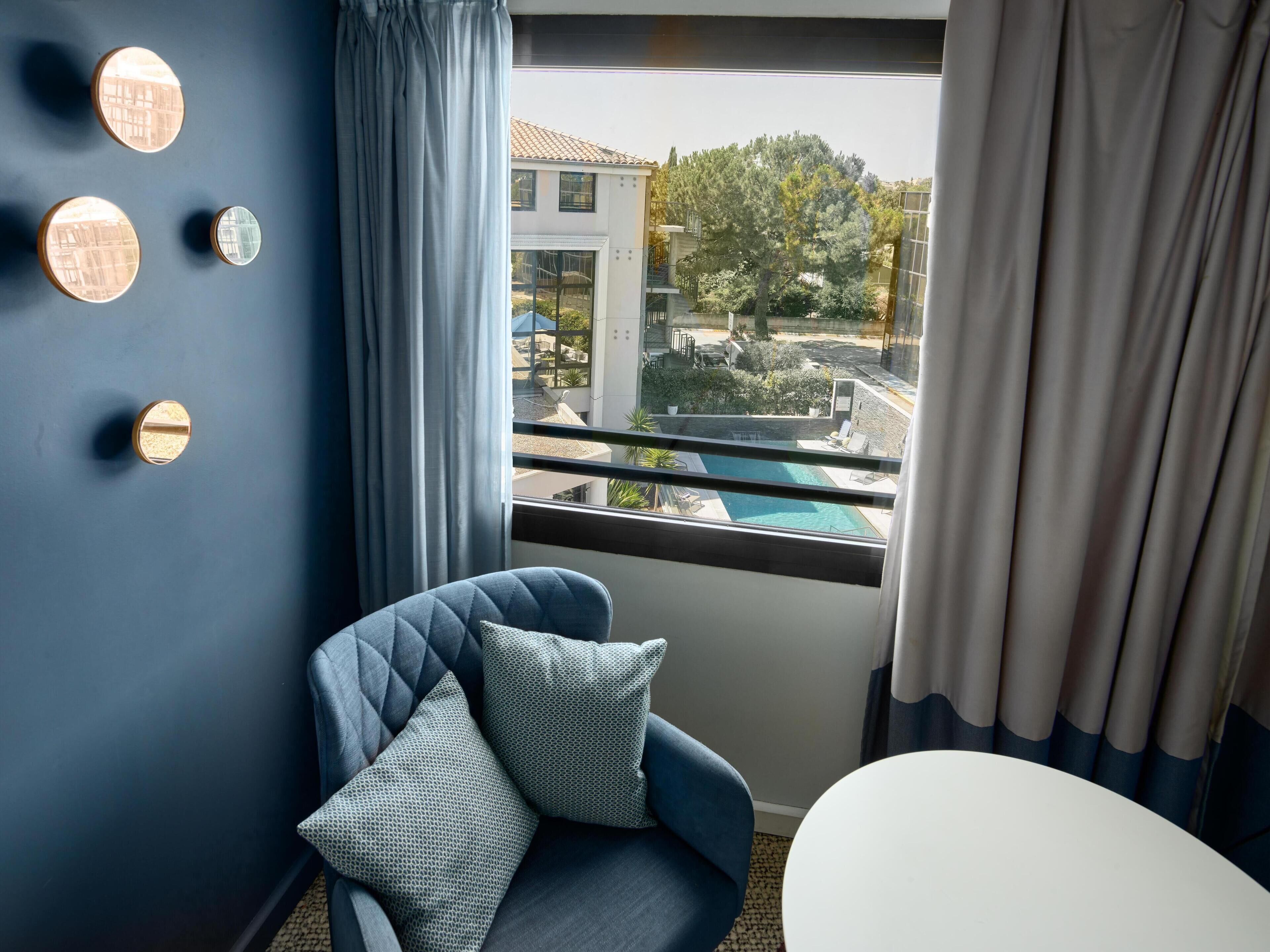 A room with a view of a swimming pool, a blue chair with a pillow, and a round table.