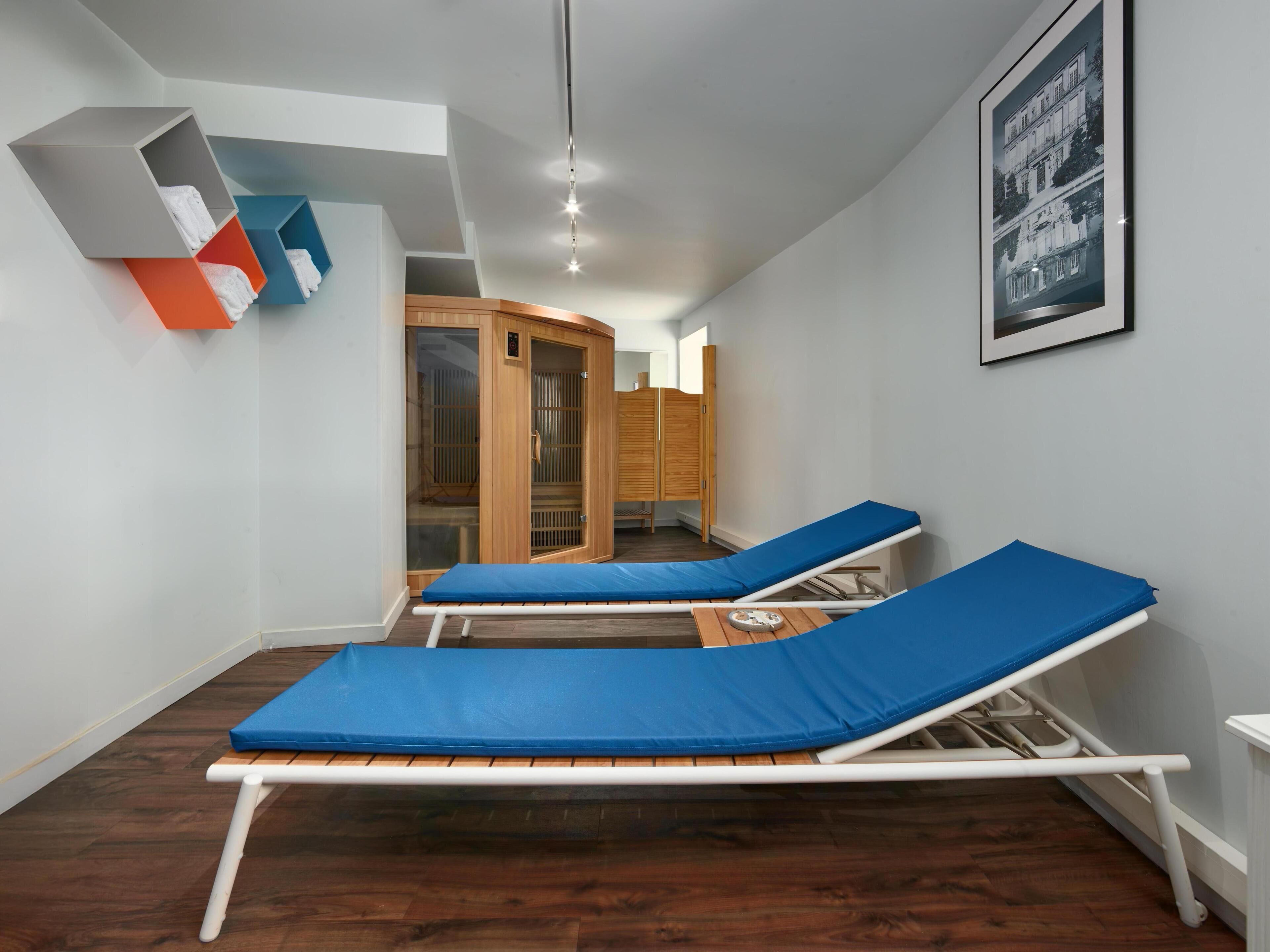 Una habitación moderna con dos camas reclinables azules, un armario de madera y un cuadro en la pared.